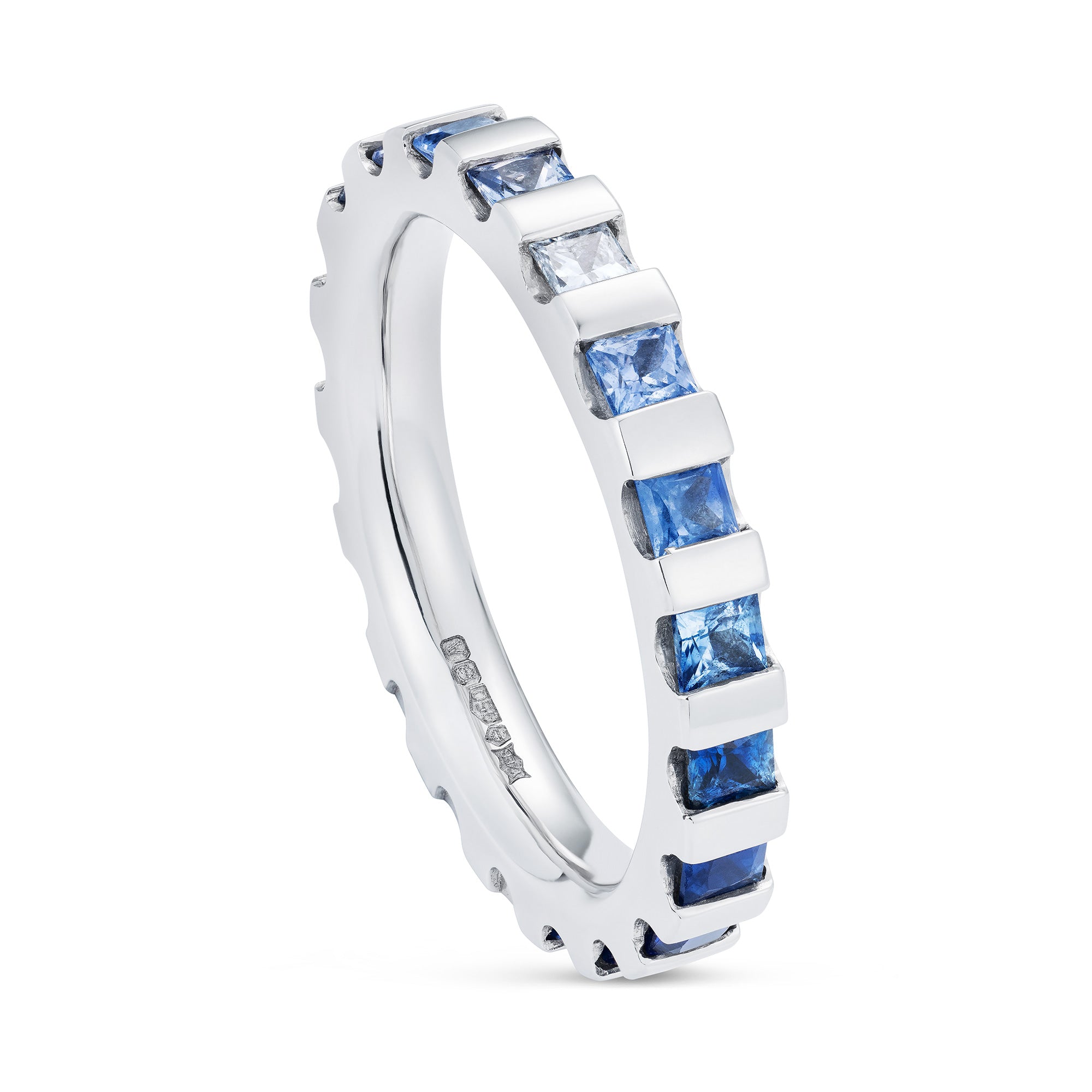 Platinum eternity ring white diamond in the centre, going out from light blue to deep blue sapphires. Angled view.