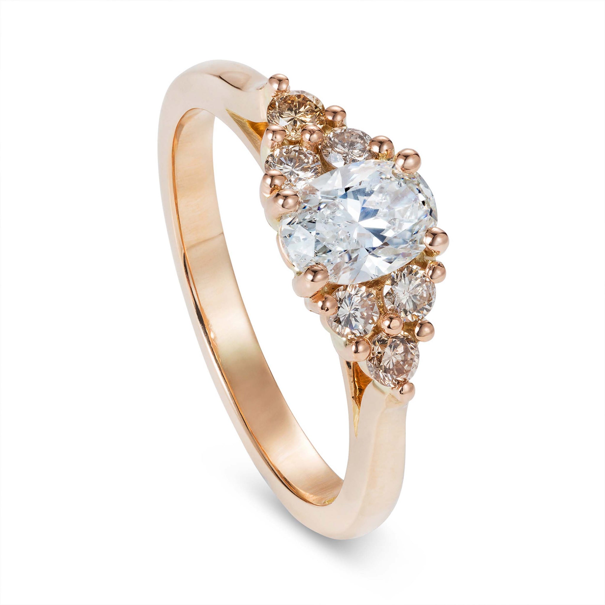 Yellow gold engagement ring with a white oval cut diamond accented by champagne and honey tone round diamonds. Designed by Yasmin Everley. Angled view.