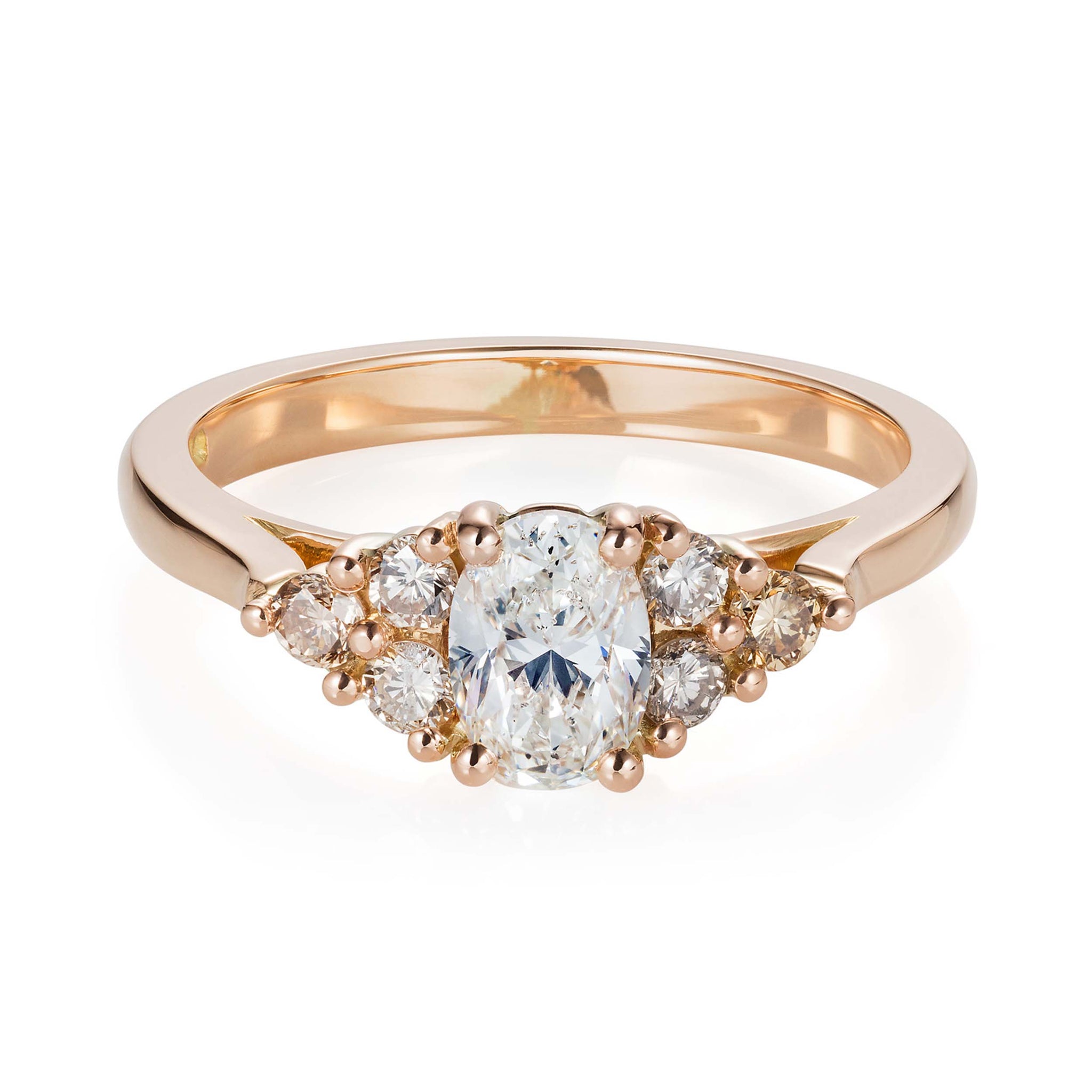 Yellow gold engagement ring with a white oval cut diamond accented by champagne and honey tone round diamonds. Designed by Yasmin Everley. Front view.